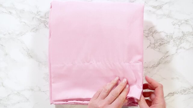Hands folding pink bedsheet neatly on marble surface