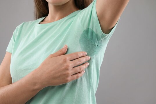 Unrecognizable young woman showing large wet sweat stain under armpit on light green t-shirt. Concept of hyperhidrosis, body odor problem, and personal hygiene