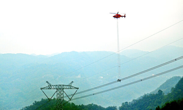 Helicopter Carries High Voltage Transmission Lines Over Mountainous Area