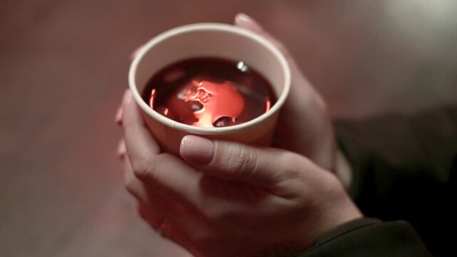 Close Up Hands Holding Hot Mulled Wine Cup in Winter Christmas Market
