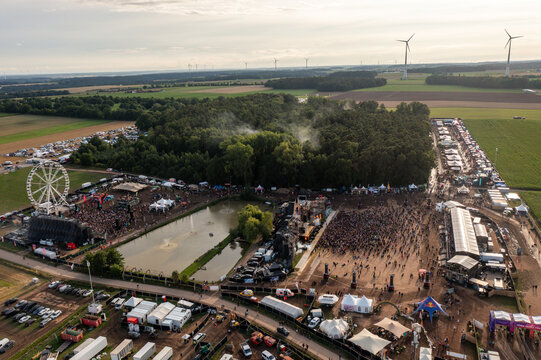 Herzogenaurach, Germany - 27 July 2025: Aerial view of Open Beatz Festival with stages, a Ferris wheel, and crowds of people surrounded by forest and wind turbines.