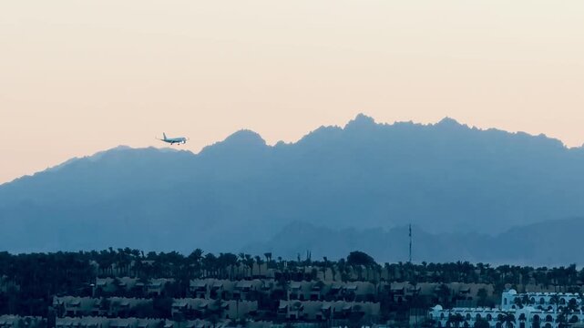 Passenger airplane cabin fuselage, wings and jet engine jetliner silhouette flying in sky. Commercial aircraft touchdown landing gear approach on background of Sinai mountains in Sharm El Sheikh.