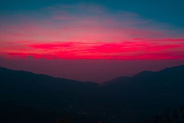 Obraz premium Dramatic sunset sky filled with vibrant pink and magenta clouds over dark mountain silhouettes. Moody evening landscape background with text space.