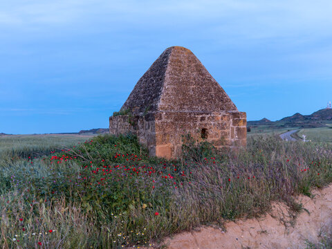 Traditional stone hut in a rural field with red poppies at twilight, beautiful countryside landscape during blue hour.