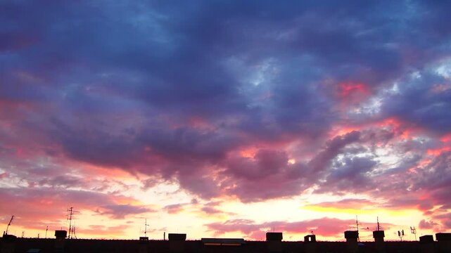 A beautiful sunset displays colorful clouds over a city skyline. The bright colors fill the sky as the sun sets behind buildings. This moment captures the changing light of dusk.