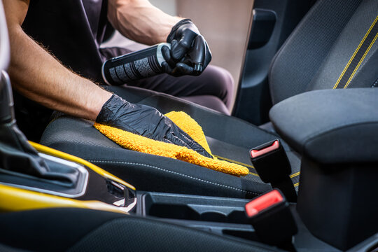 Cleaner hands cleaning car seat with yellow cloth and spray, interior car wash and vehicle cleaning concept
