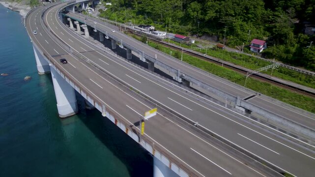 高速道路の斜め俯瞰 行き交う車両やトラックを追従する海上高架橋のドローン空撮