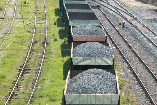 Freight wagons loaded with railway ballast gravel beside old and reconstructed rail tracks viewed from above.