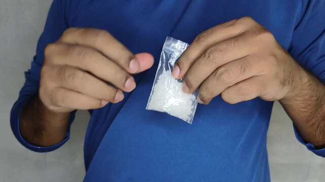 Closeup of drug addict person holding small pack of methamphetamine or crystal meth synthetic drug for quality check. Consuming illegal narcotic substance or intoxication habit in young adults concept