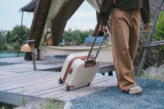 Travel insurance and eco-tourism concept traveler pulling suitcase luggage on wooden path towards glamping tent enjoying safe journey and peace of mind during nature weekend getaway vacation