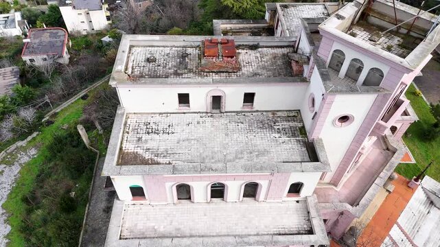 High-angle aerial shot descending over the weathered terraces, roof tiles, and arched windows of the abandoned King Zog Royal Villa historic mansion in Durres, Albania