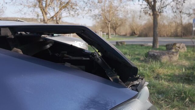 Damaged front of a dark blue car after a collision. Visible engine compartment under a wrinkled bonnet. Slow motion dolly out side view of a broken car hood.