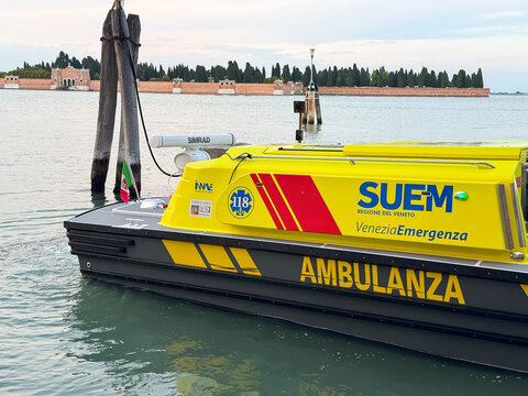 Venice, Italy - May 20, 2026: Emergency ambulance boat labeled "AMBULANZA" docked at a pier in Venice, Italy, with a scenic waterfront and trees in the background