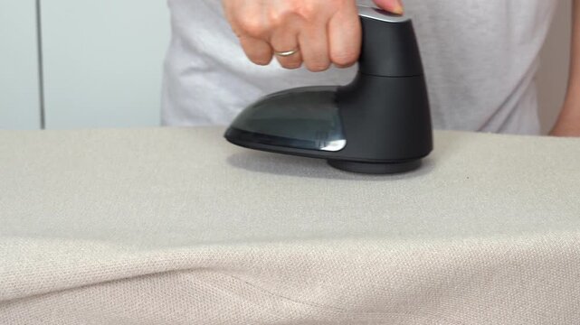 Hand removes pills from knitted clothing using fabric shaver. Textile pilling. Linting. Fabric lint, pilly, pellet, fluff. Fluff-ball remover. Household
