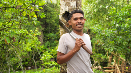 Portrait of smiling young indonesian farmer, coconut tree and machete, in rural farm of flores island, indonesia, southeast asia © Spice Footage