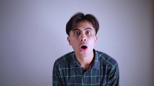 Surprised young Asian man looking at camera with funny shocked face expression, amazed guy reacting to unexpected good news or shock promo concept