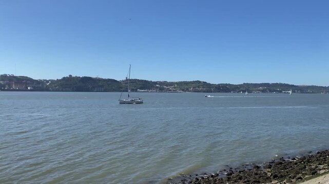 Sailing yacht and boats moving on Tagus river under clear blue sky in Lisbon Portugal