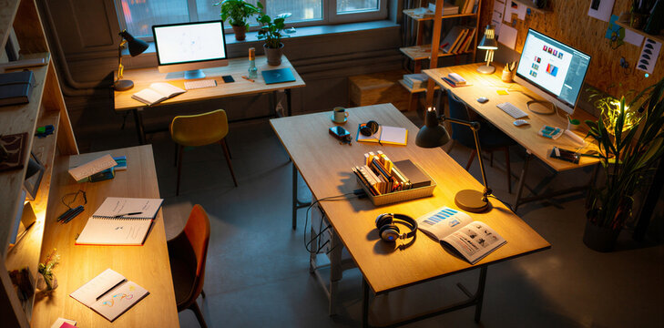 Empty creative office studio with multiple desks computers and warm lighting