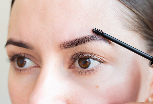 Young woman combing her eyebrows with a brush, making a beautiful shape. Eyebrow care. Eyebrow styling with gel for fixation.