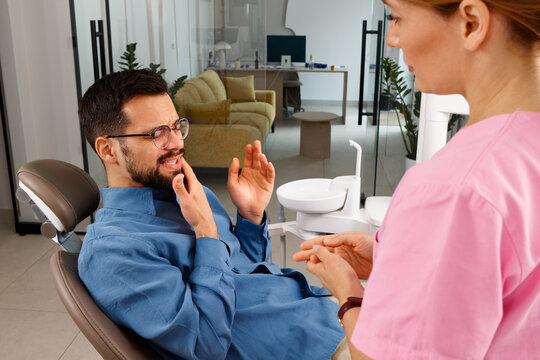 Patient experiencing tooth pain in a dental clinic explaining symptoms to a female dentist