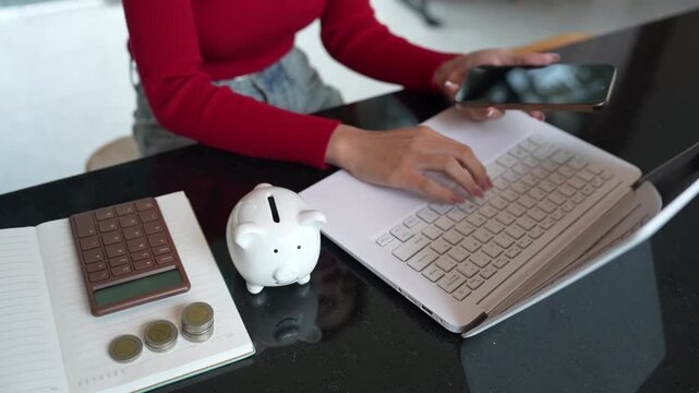 Woman using a smartphone beside a piggy bank and calculator, representing digital budgeting, saving money, and personal financial management.
