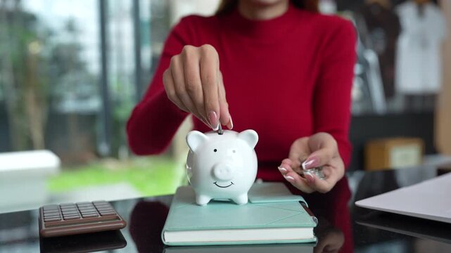 Close-up of a woman putting coins into a white piggy bank, representing saving money, personal finance, budgeting, and future financial security.