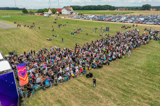 Herzogenaurach, Germany - 25 July 2025: Aerial view of the Open Beatz Festival entrance with a large crowd of people queuing on a green field next to a parking lot and rural buildings.
