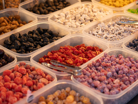 Close-up of various colorful preserved plums and dried fruits in trays at a street food market.