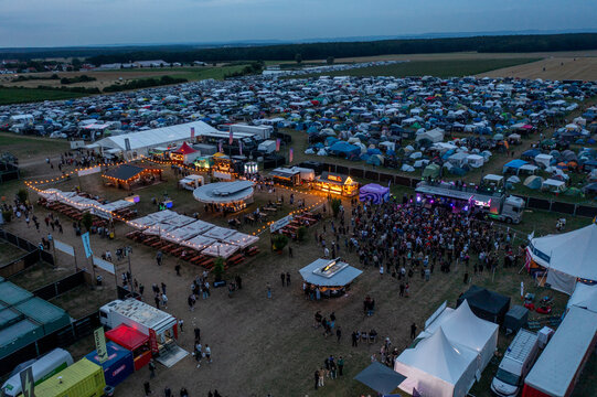 Herzogenaurach, Germany - 25 July 2025: Aerial view of Open Beatz Festival featuring a large campsite with colorful tents, food stalls, and crowds of people at dusk.