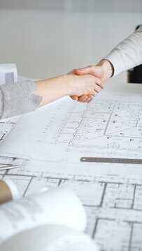 Handshaking between two architects finalizing a construction project deal, business partners agreeing on engineering blueprints and architectural models in an office, close up