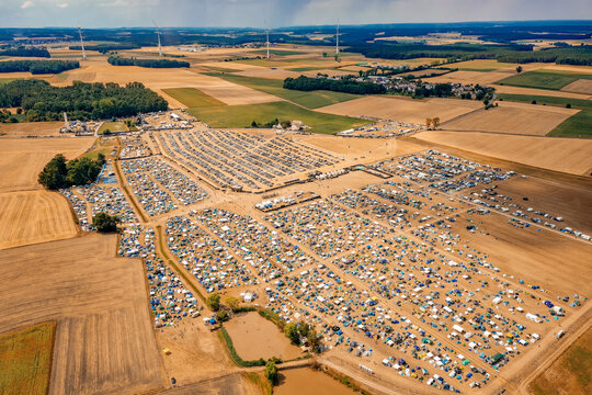 Herzogenaurach, Germany - 22 July 2022: Aerial view of the Open Beatz Festival campsite with thousands of tents and cars parked in fields surrounded by forests and wind turbines.