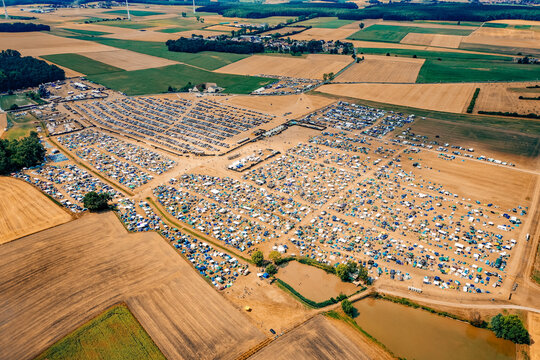 Herzogenaurach, Germany - 22 July 2022: Aerial view of the Open Beatz Festival campsite with numerous tents and parked cars surrounded by vast agricultural fields and green forests.