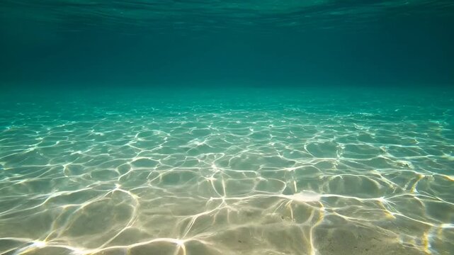 Crystal clear ocean water refracts sunlight onto a sandy seabed, creating a mesmerizing dance of light and shadow in this serene underwater scene.