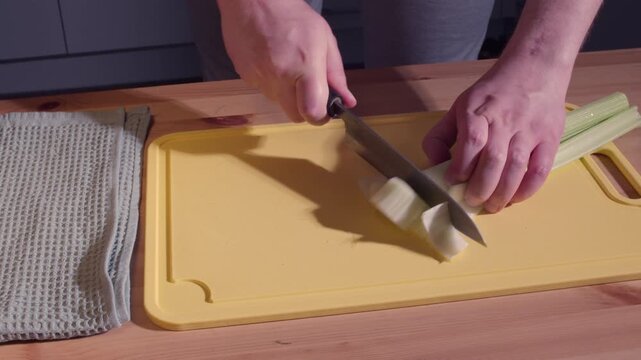 Man Cutting Celery Stalks with Japanese Knife on Yellow Cutting Board