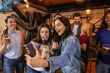 Fototapeta premium Friends singing karaoke in modern pub with beer and microphone