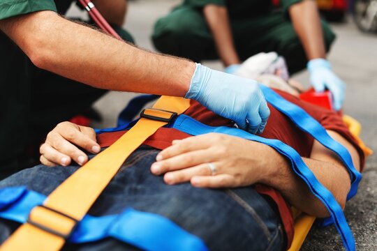 Emergency responders assist an injured person on a stretcher. Medical team secures patient with straps. Urgent care and safety in action. Healthcare concept.
