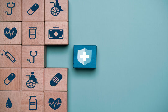 Healthcare insurance and medical protection concept with wooden blocks showing hospital, vaccine, syringe and wellness icons beside shield symbol. Health coverage and patient care concept.