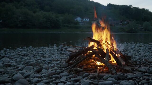 4K footage showing a campfire in the right part of the frame from a more distant viewpoint on the Drina River shore at sunset, filmed from the Serbian bank with Bosnia and Herzegovina mountains behind