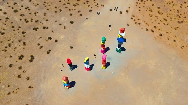 Rising over seven stacks of brightly-painted boulders in the desert. Some people walk around the art installation in Seven Magic Mountains, Las Vegas, Nevada, USA.