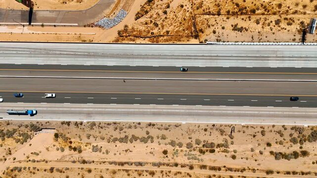 Desert covered with lichens and shrubs is crossed by the highway. Lots of cars move by the multi-lane motorway. Top view.