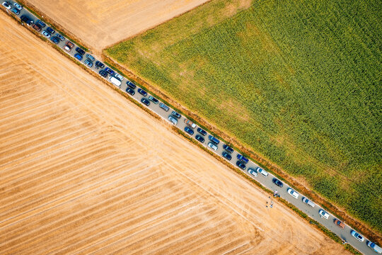 Herzogenaurach, Germany - 22 July 2022: Aerial view of a long line of cars parked on a narrow road between agricultural fields during the Open Beatz Festival.