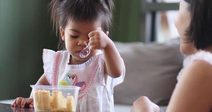 Child feeding snack independently, A little child feeds itself, while mother claps her hands, expressing family love, learning, care, and warm bonding moments, Thai Asian