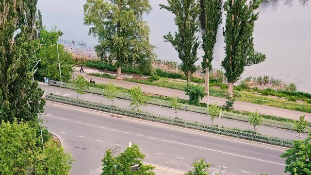 High angle timelapse of city traffic on a scenic road near a river canal with lush green poplar trees