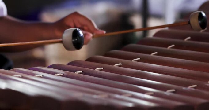 Hands playing a wooden xylophone with mallets, outdoors at night market, Showcasing traditional music culture, close-up