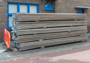 laying wooden scaffolding planks stacked outside on the sidewalk in a street © JADA