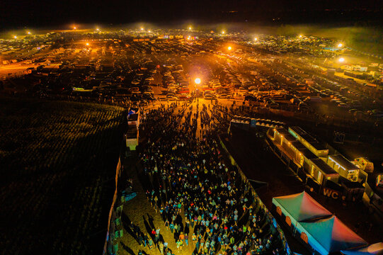 Herzogenaurach, Germany - 22 July 2022: Aerial view of the Open Beatz Festival at night with a large crowd of people, bright stage lights, and a vast camping area under a dark sky.