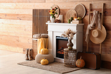 Fototapeta premium Interior of living room with folding screen, ladder, suitcase, wicker table and autumn decorations on fireplace near wooden wall