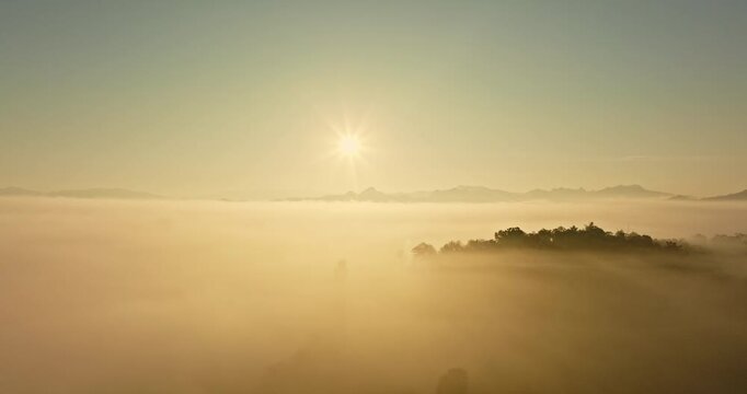Panoramic view of a tranquil valley wrapped in morning mist as sunlight paints the sky with vibrant golden tones during dawn.