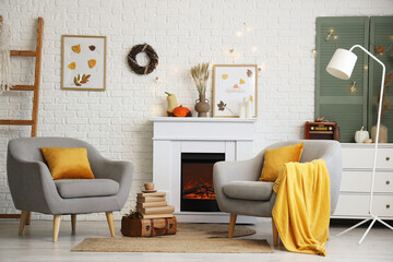 Fototapeta premium Armchairs, fireplace and autumn decor in interior of living room