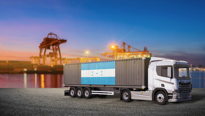 Container Truck at Port at Dusk: A modern container truck, carrying a cargo container adorned with a flag, stands on the tarmac of a bustling port during the twilight hour. © bao